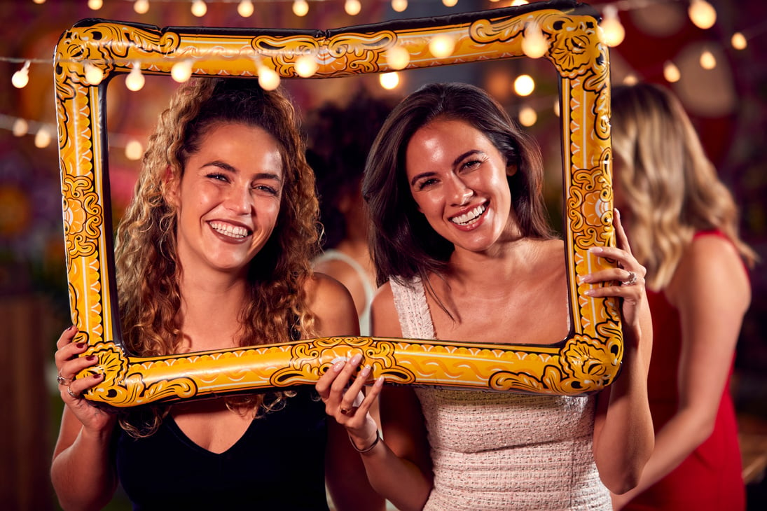 Female Friends Having Fun Posing with Photo Booth Photo Frame at Party in Bar